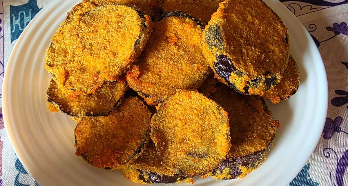 Fette dorate di melanzane in friggitrice ad aria, impanate e croccanti, servite su un piatto bianco.