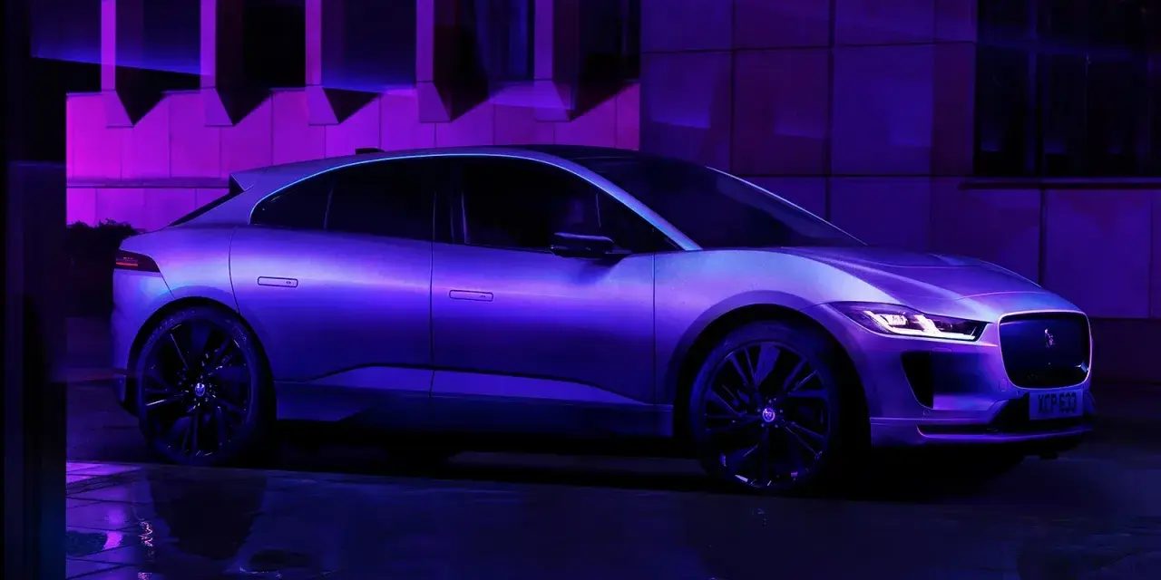 Jaguar I-Pace w fioletowym świetle, zaparkowany na mokrej nawierzchni.