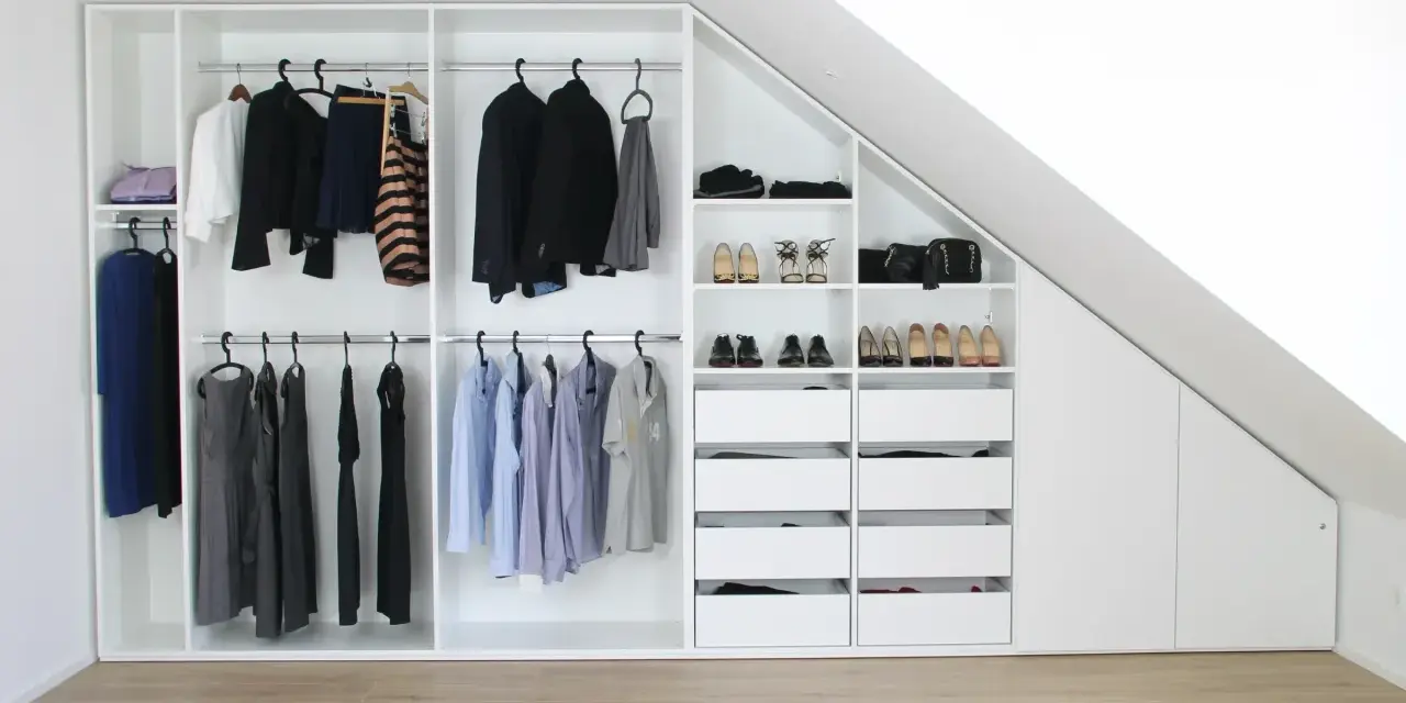 Einbauschrank selber bauen: Weißer Schrank mit Kleiderstangen, Schubladen und Schuhfächern unter einer Dachschräge.