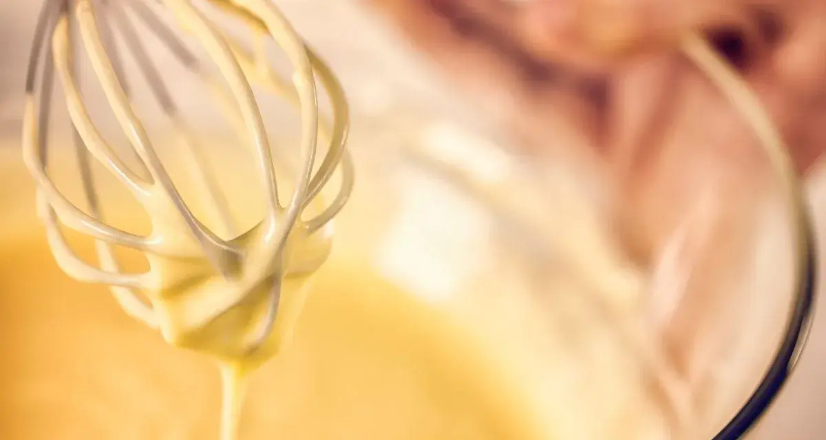 Frusta da cucina che raccoglie una densa pastella per fritti, pronta per creare delizie croccanti.