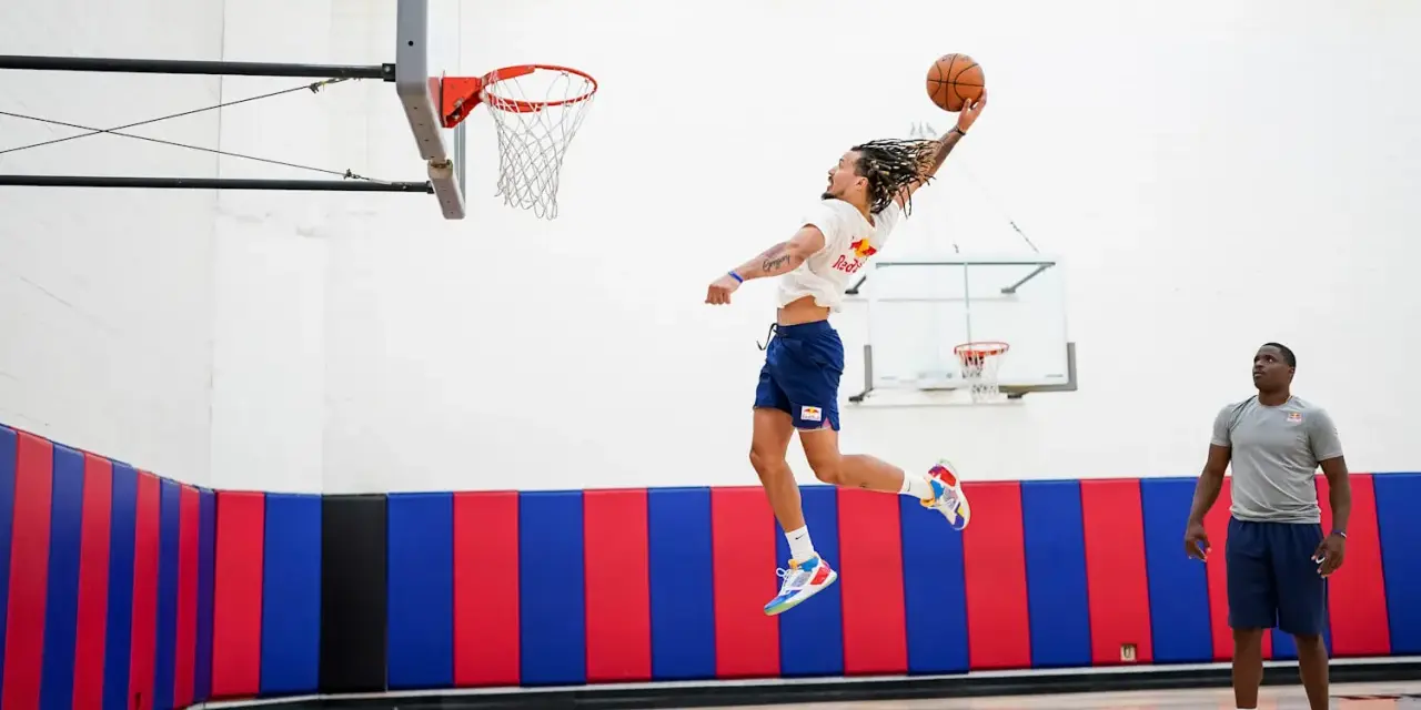 Un joueur de basket-ball en plein saut, ballon en main, effectue un exercice de pliométrie. Un autre joueur observe.