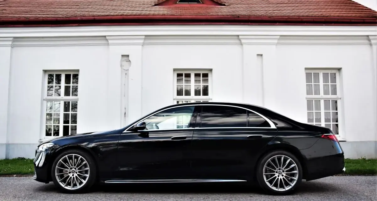 Elegancki, czarny Mercedes S500 lśni na tle białej, zabytkowej fasady z czerwonym dachem.