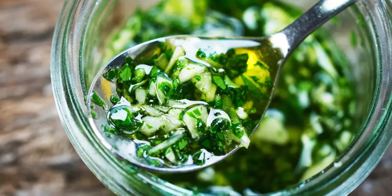 Łyżka z aromatycznym, zielonym sosem chimichurri, pełnym ziół i czosnku, zanurzona w słoiku.