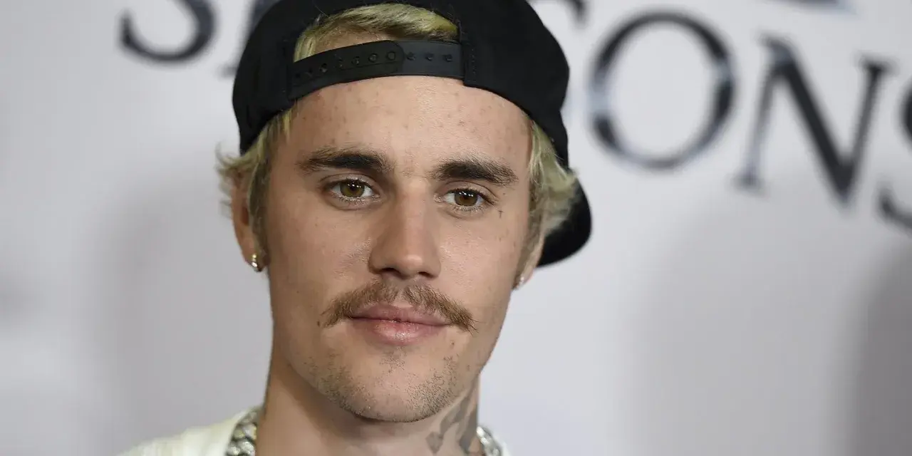 Justin Bieber con un gorra negra y un bigote herradura, luciendo una cadena plateada.