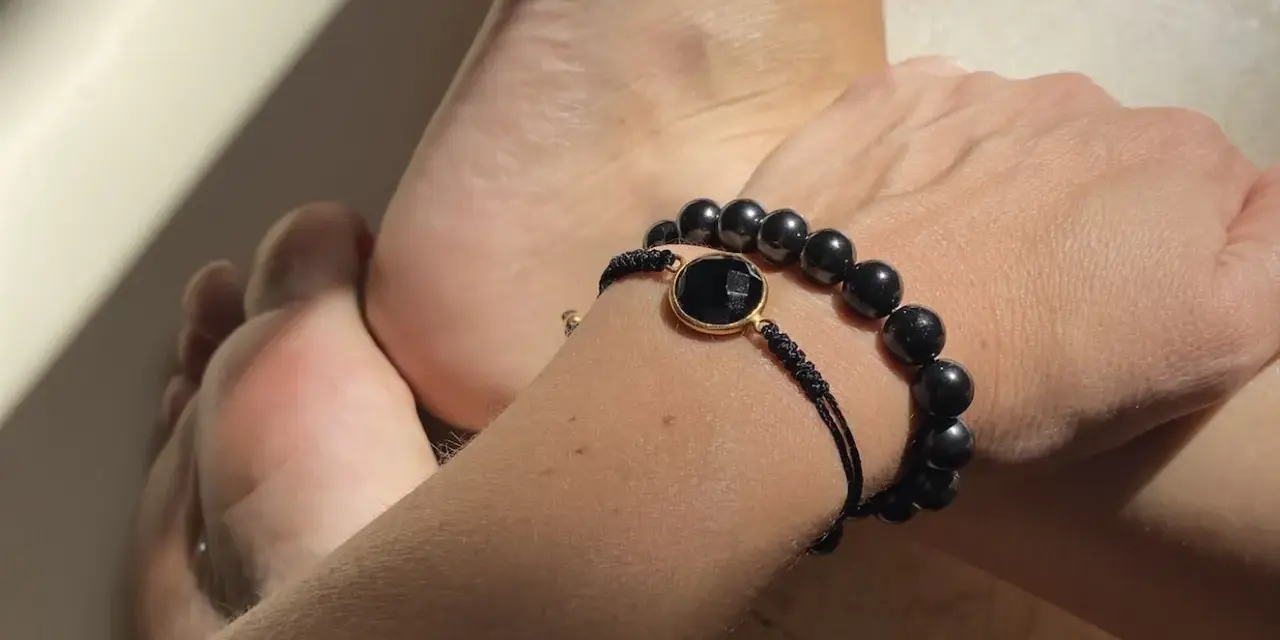 Pulsera con cuentas de obsidiana, una piedra negra protectora, junto a unos pies.