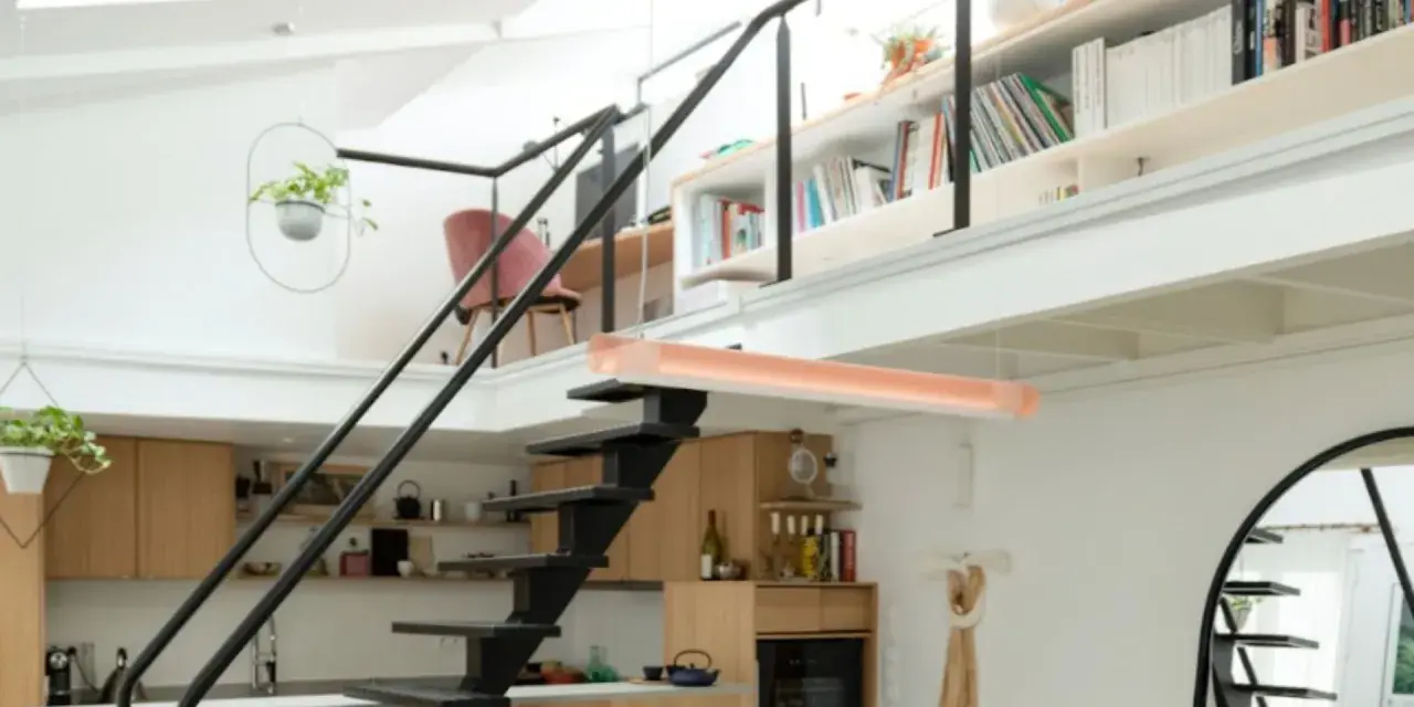 Aménagement mezzanine ouverte avec escalier métallique, cuisine en bois, étagères remplies de livres et plantes suspendues.