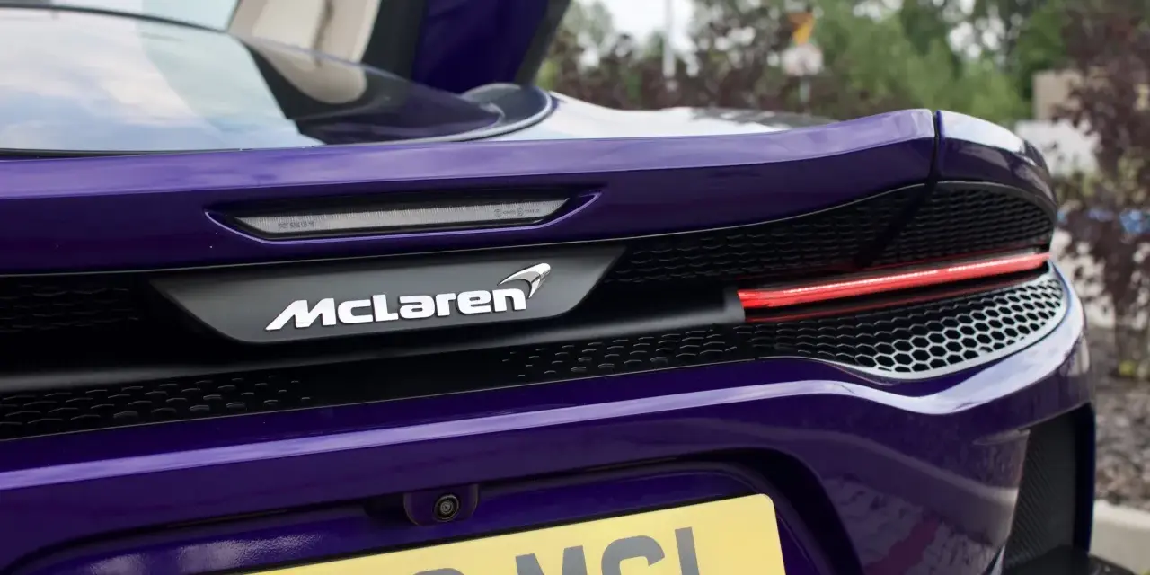Fioletowy McLaren GT z otwartymi drzwiami, widok na tył z logo i tablicą rejestracyjną.