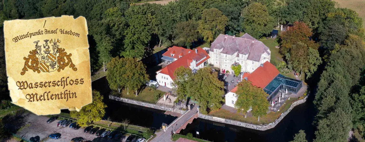 Luftaufnahme des Wasserschlosses Mellenthin mit Wassergraben, Brücke und umliegendem Park. Der Eintritt ist frei zugänglich.