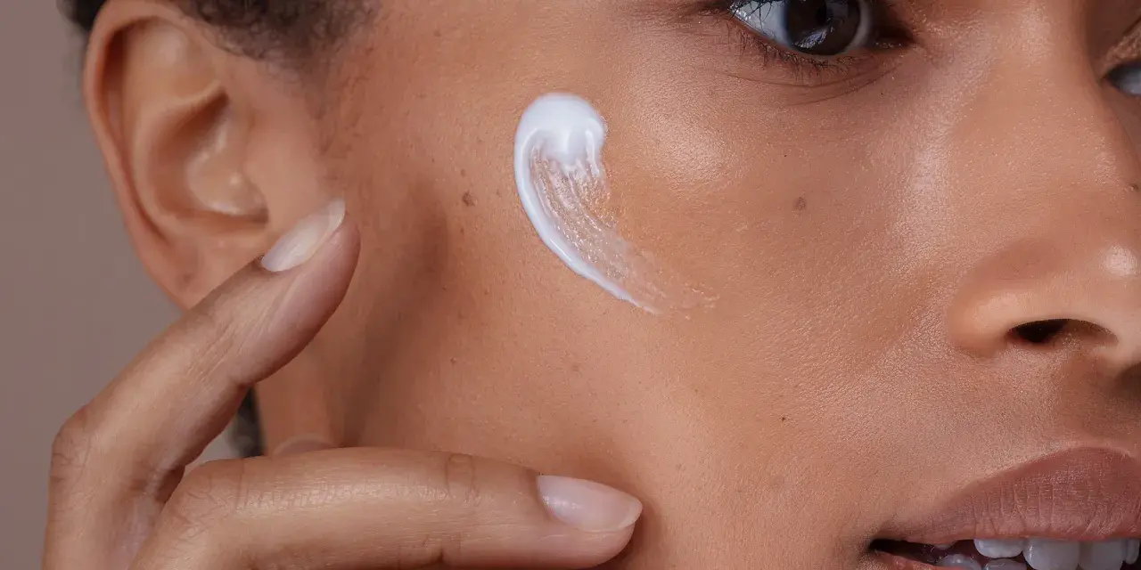 Creme wird auf die Wange einer Person mit fettiger, unreiner Haut aufgetragen.