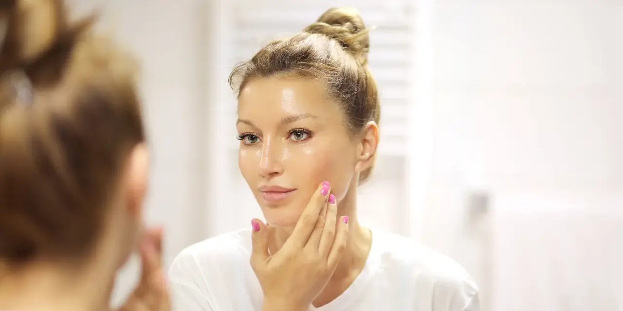 Donna con capelli raccolti applica un siero sul viso. La domanda è: quanti sieri si possono usare insieme per una pelle luminosa?