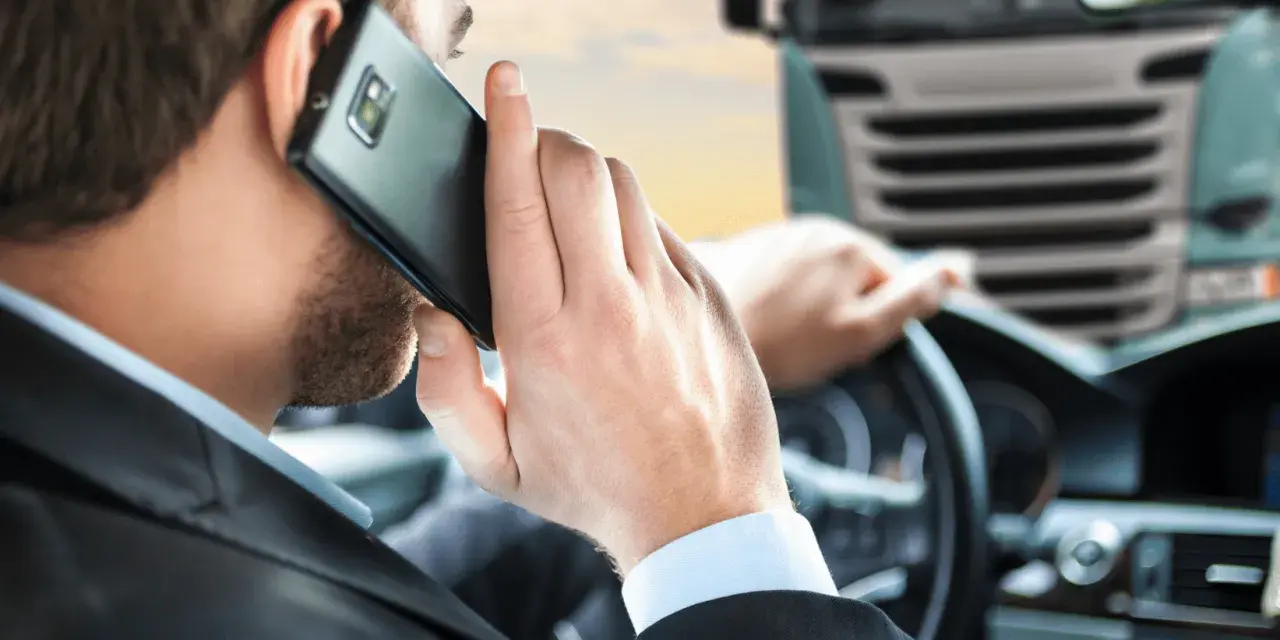 Biznesmen w garniturze rozmawia przez telefon, siedząc za kierownicą ciężarówki. To symbol odpowiedzialności spedytora.