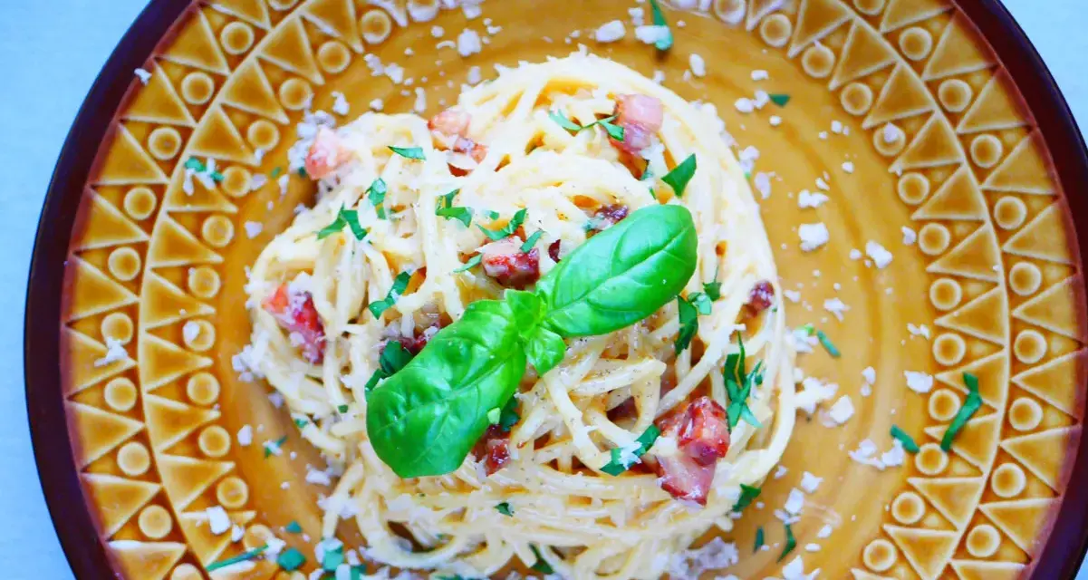 Pyszna carbonara ze szparagami, udekorowana bazylią i posypana parmezanem, na ozdobnym talerzu.