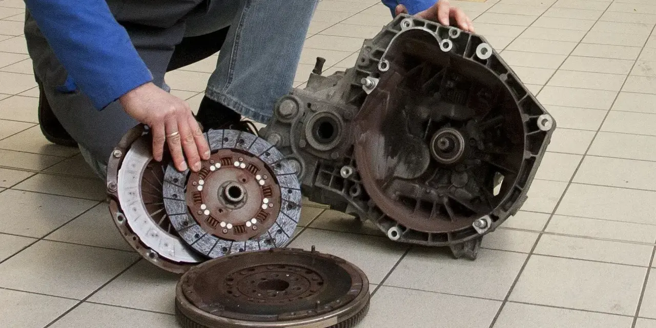 Mechanik prezentuje części po demontażu skrzyni biegów, przygotowując się do wymiany łożyska oporowego.
