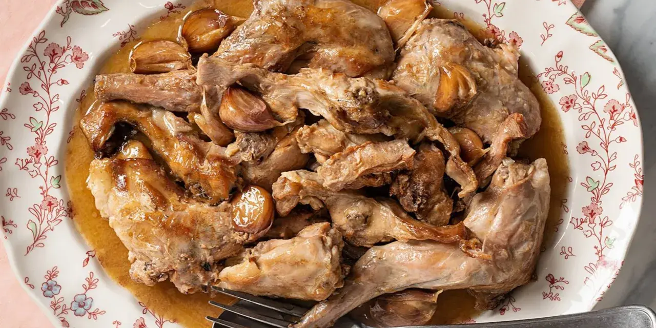 Conejo al ajillo servido en un plato con borde floral, con trozos de carne dorada y dientes de ajo enteros.