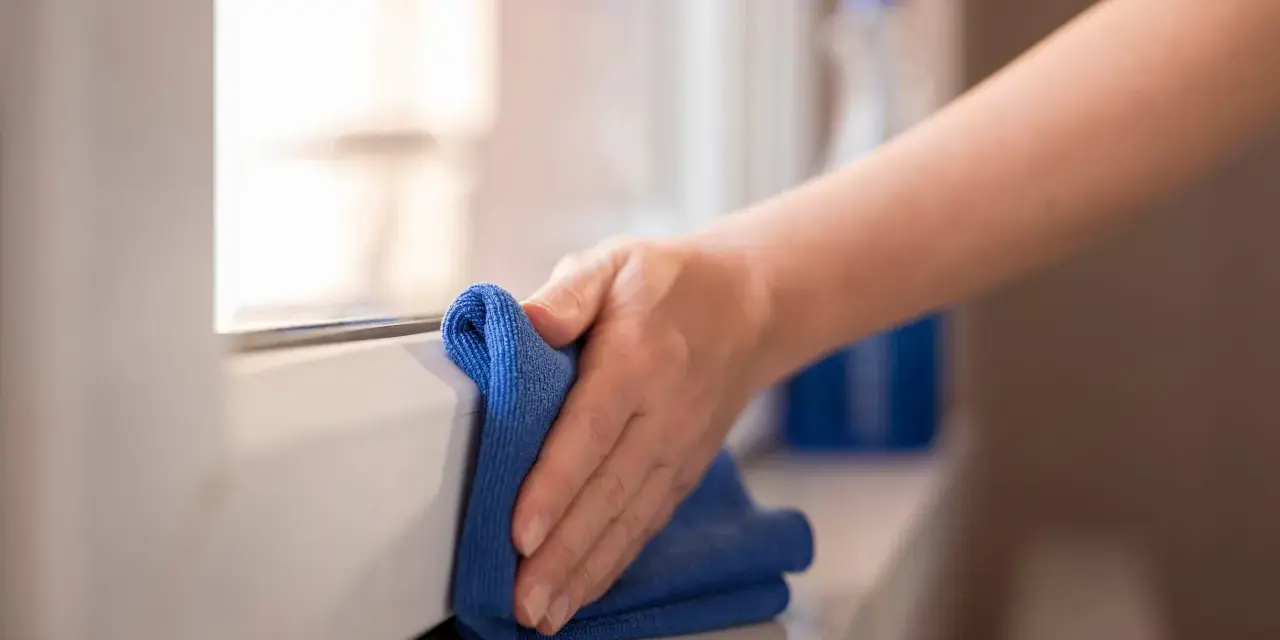 Mano pulisce davanzale in PVC effetto legno con panno blu. Scopri come pulire pvc effetto legno per mantenerlo come nuovo.