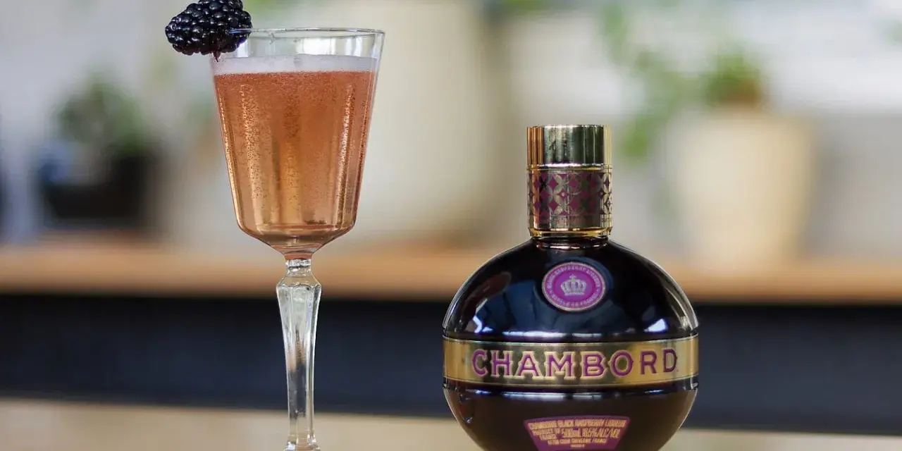 Chambord likier jak pić? Elegancki kieliszek z różowym drinkiem i jeżyną obok butelki likieru. Idealny na specjalne okazje.