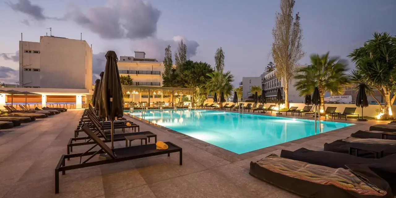 Basen hotelowy oświetlony nocą, leżaki i palmy. Idealne miejsce na relaks, zgodnie z licznymi heronissos hotel opinie.
