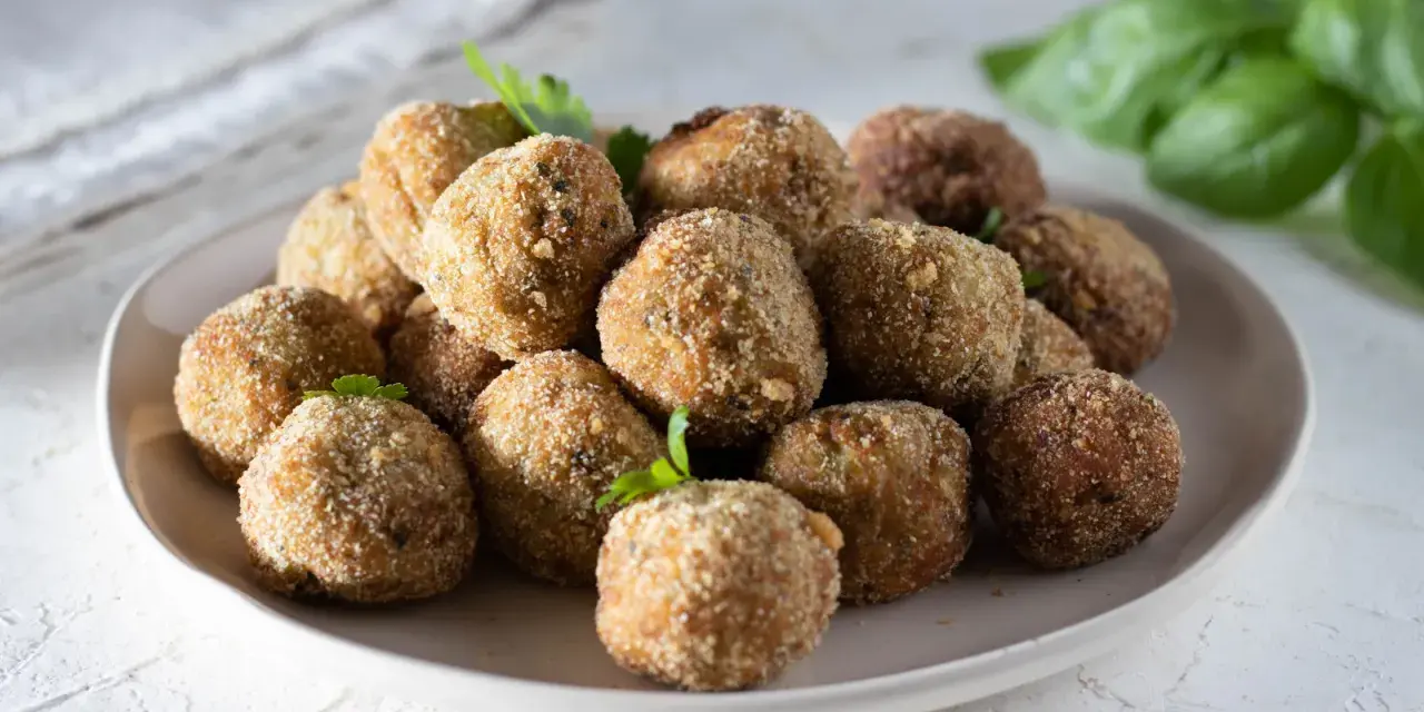 Un piatto pieno di polpette di melanzane dorate e croccanti, guarnite con prezzemolo fresco.