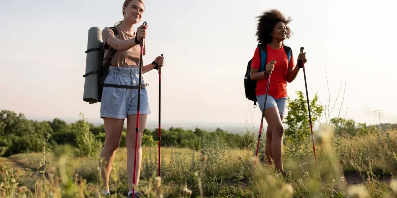 Zwei Frauen genießen das Wandern mit nur einem Stock auf einem sonnigen Hügel.