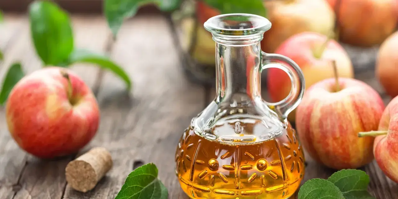 Aceto di mele in un decanter, mele rosse e foglie verdi su un tavolo di legno. Un rimedio naturale per sapere come eliminare i funghi della pelle velocemente.