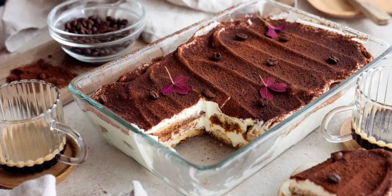 En krämig tiramisu i glasform, perfekt för ett enkelt tiramisu recept. Toppad med kakao, kaffebönor och lila blommor.
