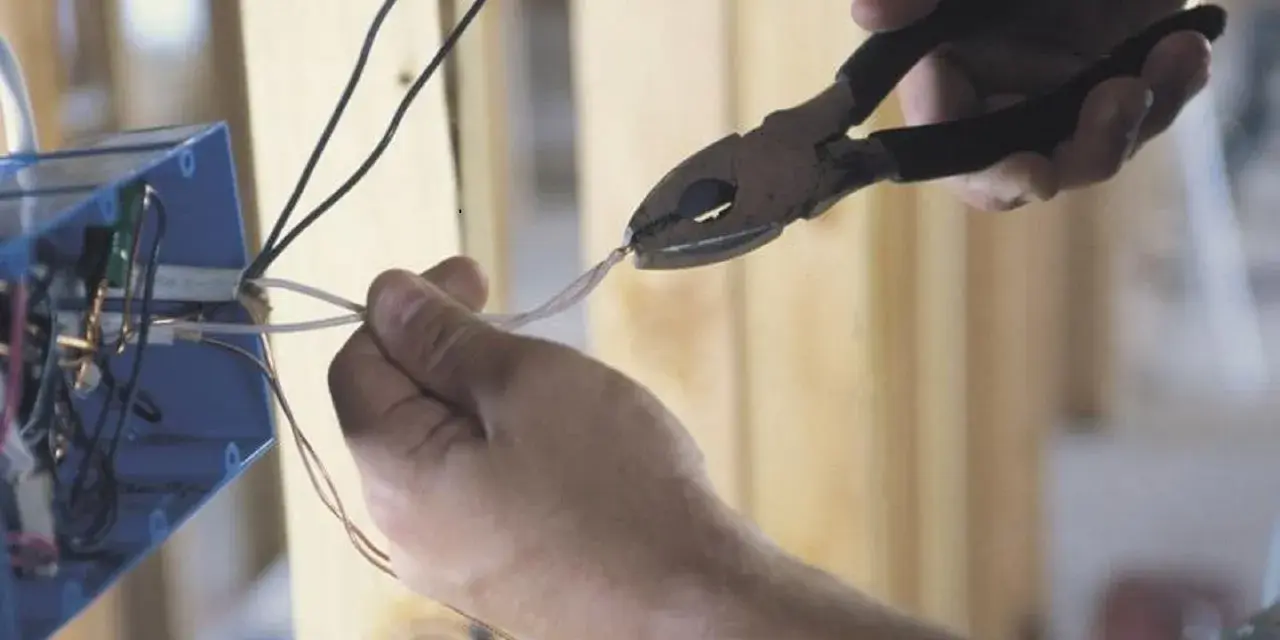 Ręce przycinają przewody do skrzynki elektrycznej. To kluczowy krok, by dowiedzieć się, jak zostać elektrykiem.