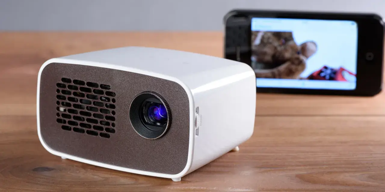 Kleiner Beamer mit Handy verbinden für Heimkino. Ein Smartphone zeigt ein Bild, während der Beamer bereit ist.