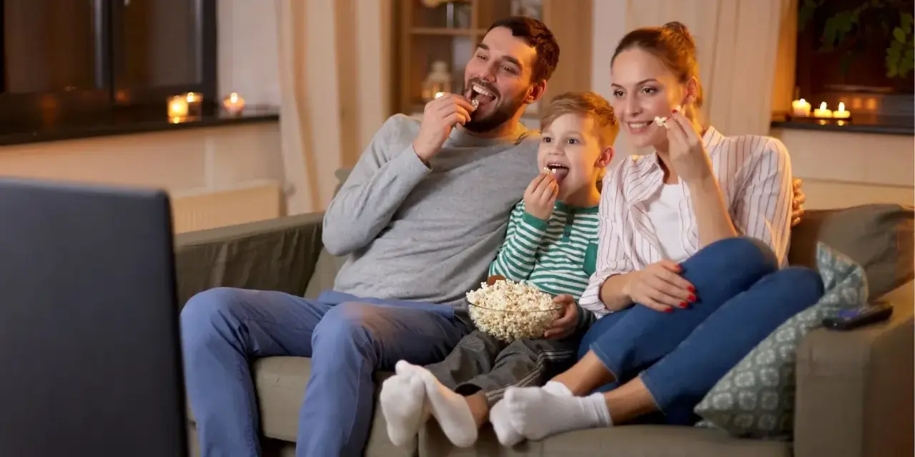 Rodzina zajada popcorn podczas oglądania filmów familijnych.