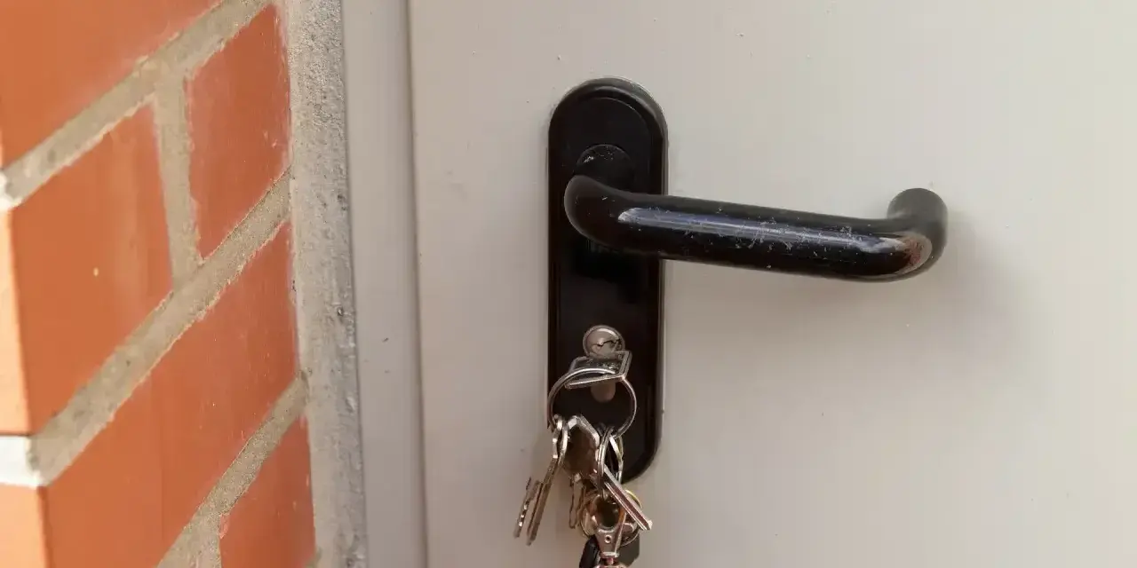 Klucze wiszą przy zamku w białych drzwiach. Zastanawiasz się, ile kosztuje wymiana zamka w drzwiach?