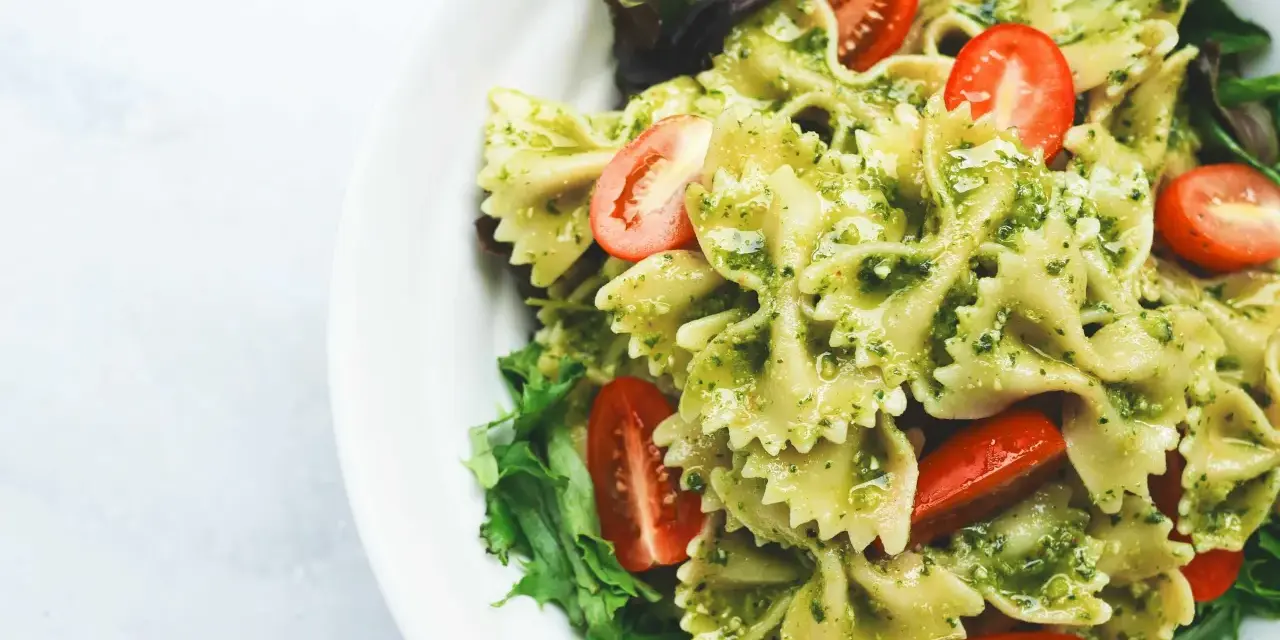 Ein köstlicher Nudelsalat mit Pesto, garniert mit frischen Kirschtomaten und Salatblättern.