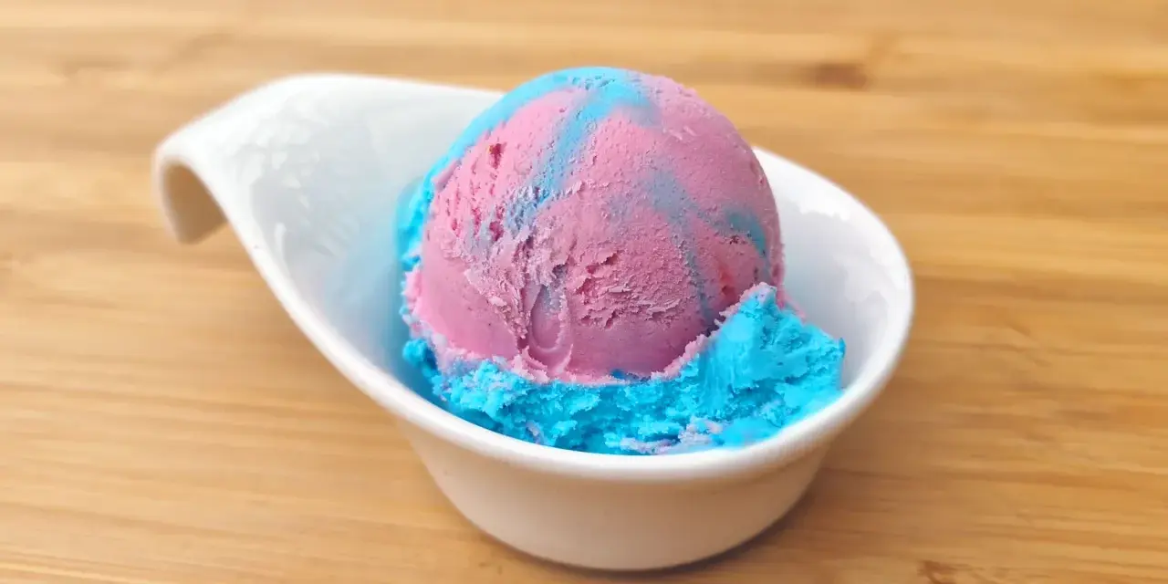 Ein Löffel eis mit kaugummi Geschmack, in rosa und blau, serviert in einer weißen Schale auf Holzuntergrund.