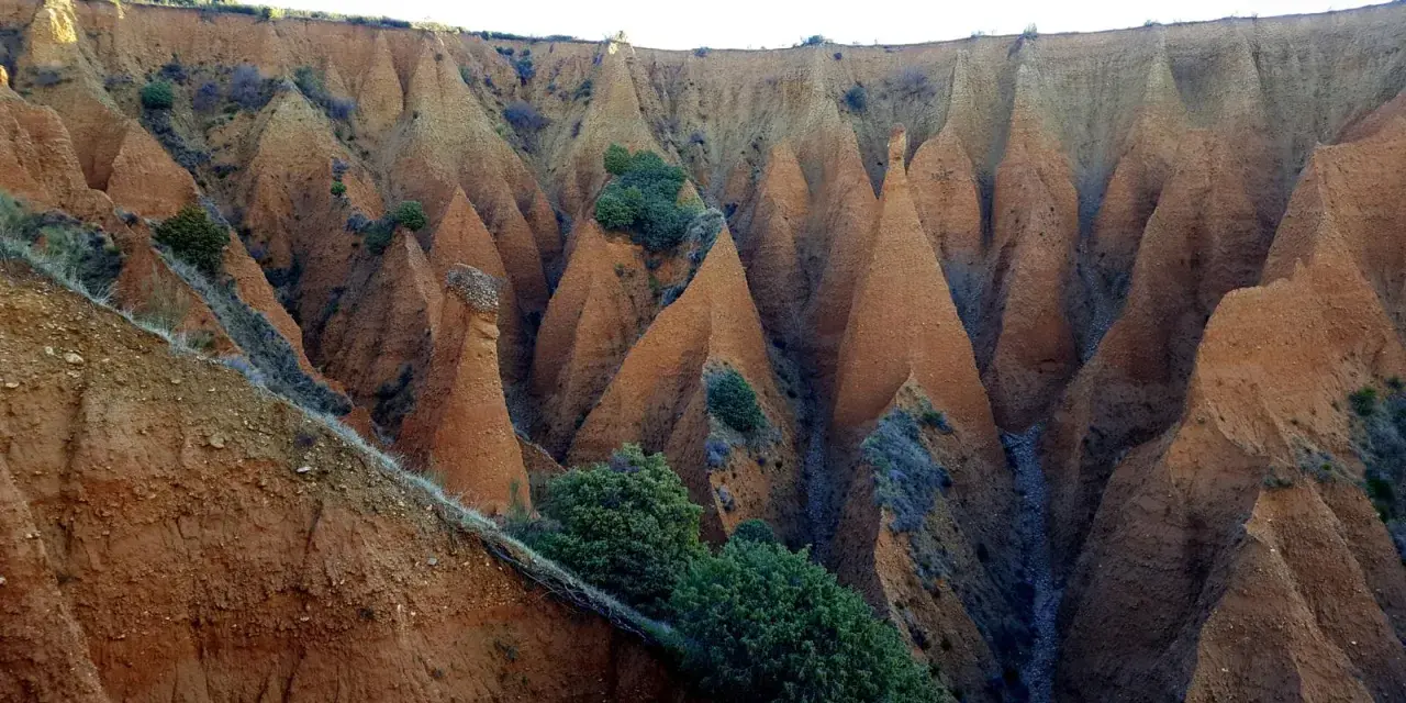 Paisaje erosionado con formaciones cónicas de tierra rojiza, vegetación escasa y un camino que parece el pontón de la oliva ruta circular.
