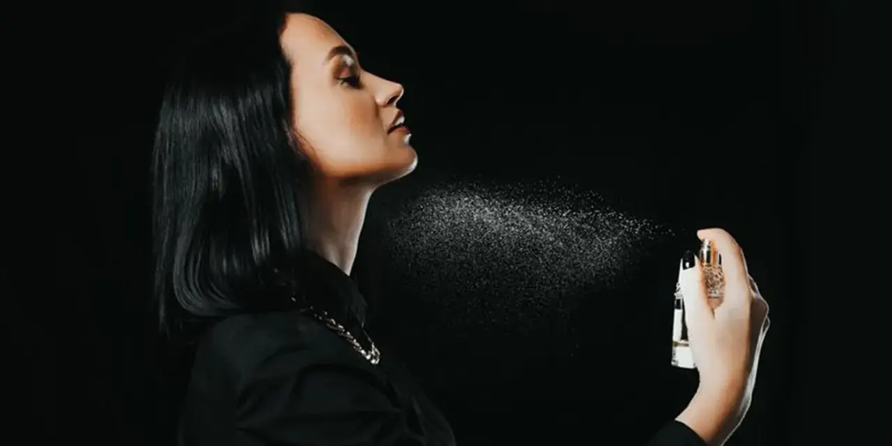 Kobieta rozpyla perfumy na szyję na czarnym tle.
