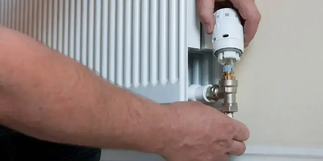 Wymiana zaworu w grzejniku bez spuszczania wody. Ręce majsterkowicza przykręcają nowy zawór termostatyczny.
