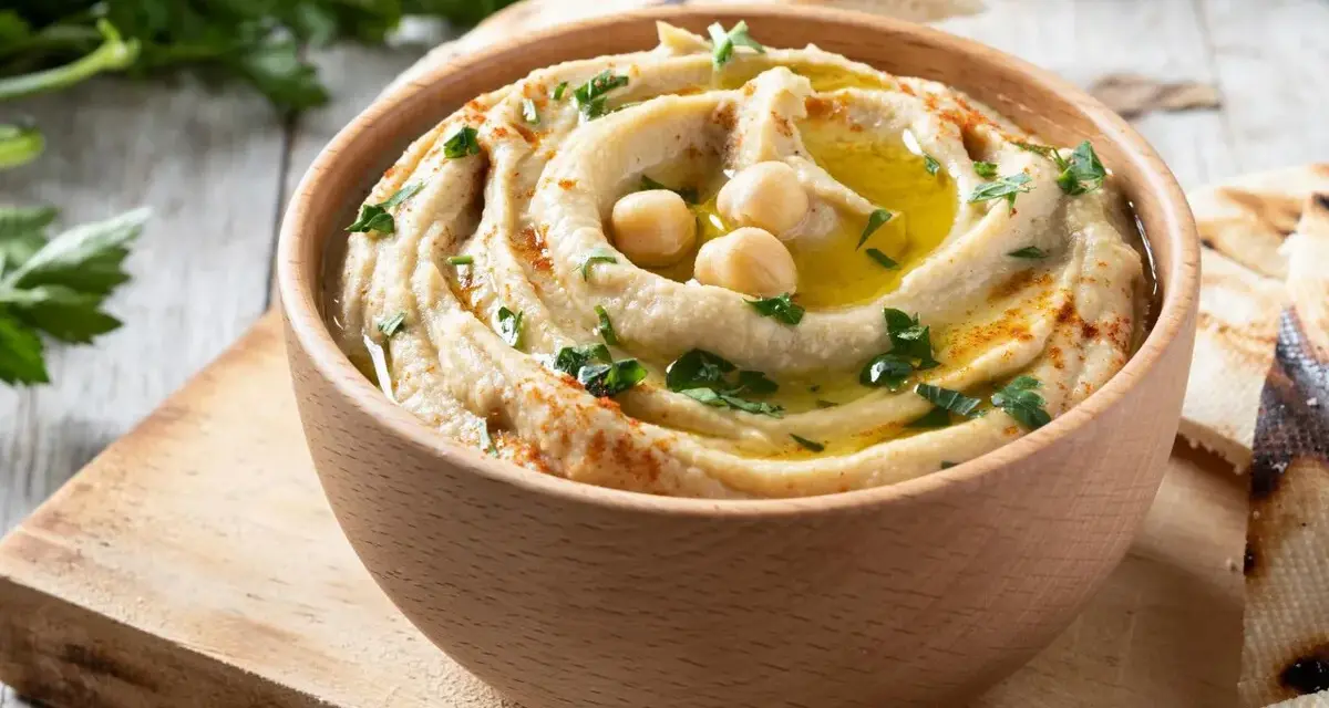 Hummus cremoso en cuenco de madera, decorado con garbanzos, aceite de oliva, perejil y pimentón.