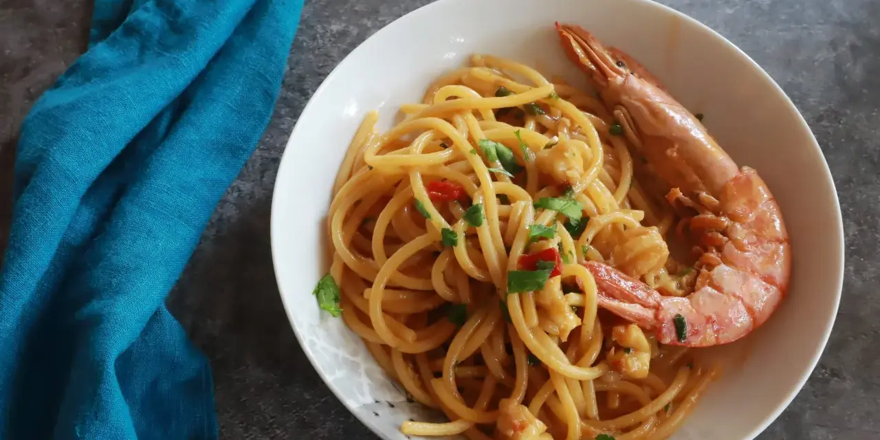 Spaghetti con gamberoni surgelati, un piatto gustoso e veloce. Un gamberone intero adorna la pasta condita con pomodorini e prezzemolo.