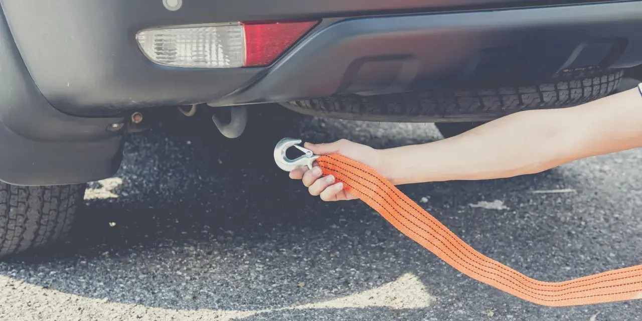 Dłoń mocuje hak liny holowniczej do haka holowniczego auta. To pokazuje, czy można holować auto na linie.