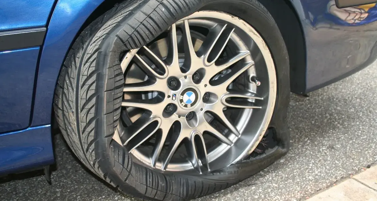Un pneumatico squarciato sul cerchione di un'auto blu. La gomma è completamente sgonfia e deformata, mostrando il danno.