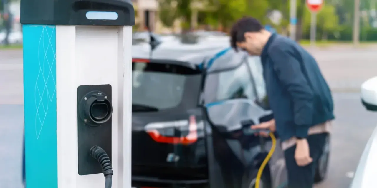 Mój elektryk czeka na ładowanie. Mężczyzna podłącza kabel do samochodu przy stacji ładowania.