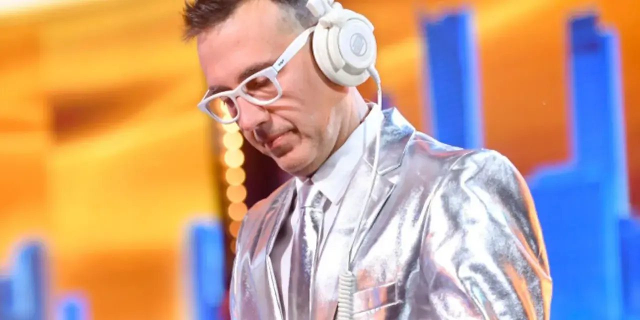 DJ w błyszczącej marynarce i białych okularach, słuchawki na uszach, gotowy do zagrania "Jaka to melodia".