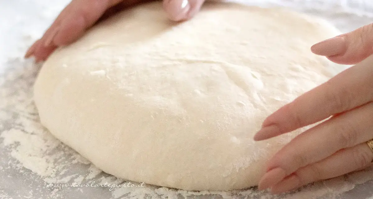 Mani che lavorano un impasto pizza veloce, soffice e pronto per essere steso.