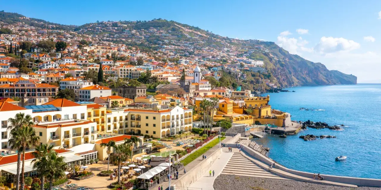 Widok na Funchal, stolicę Madery, z kolorowymi budynkami wznoszącymi się na zboczu góry, otoczonymi błękitnym oceanem.
