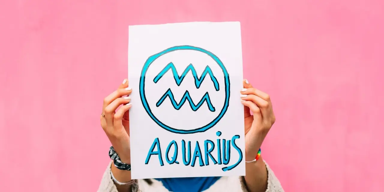 Waga i Wodnik: przyjaźń w kolorach tęczy. Ręce trzymają plakat z symbolem Wodnika i napisem "Aquarius" na różowym tle.