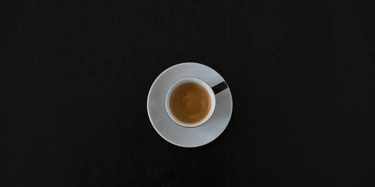 Czarna filiżanka espresso na białym spodeczku na ciemnym tle. Może symbolizować początek walki z objawami odstawienia kofeiny.