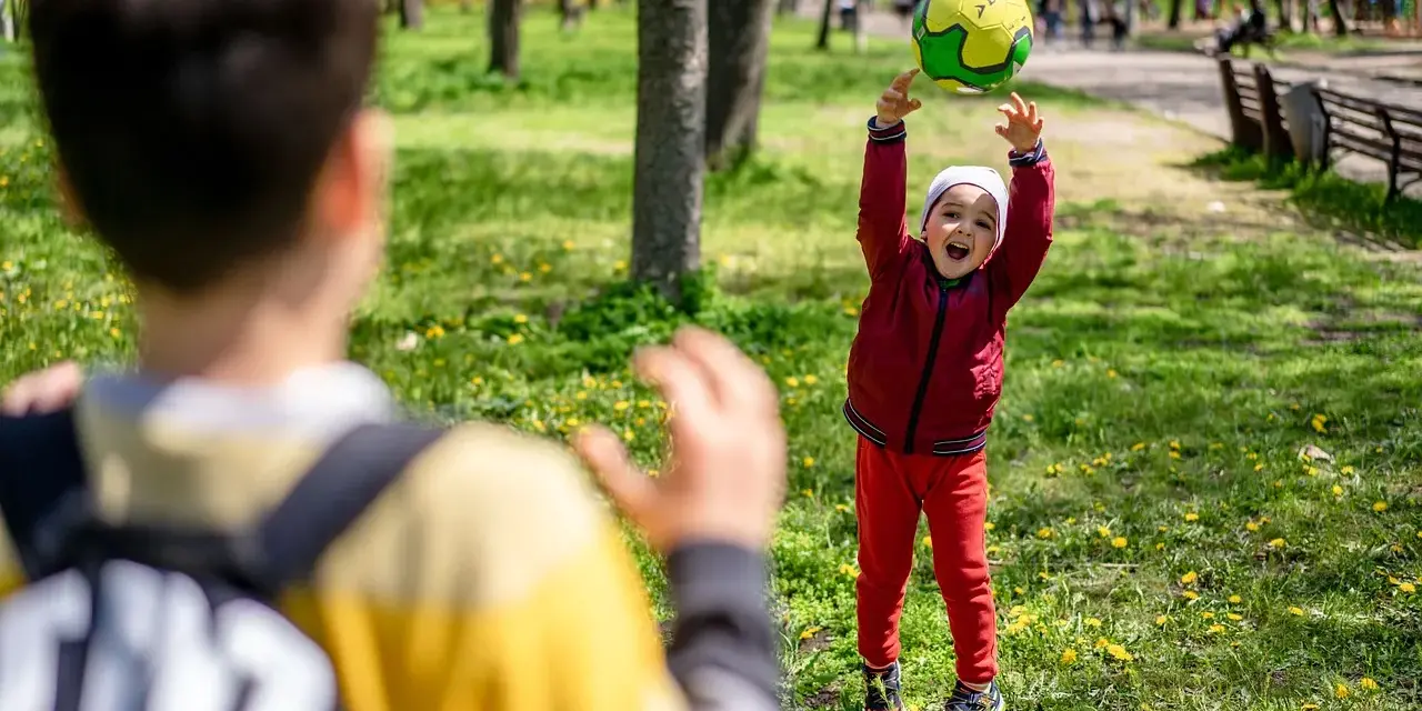 Un enfant joyeux lance un ballon en l'air dans un parc, un autre enfant est devant.
