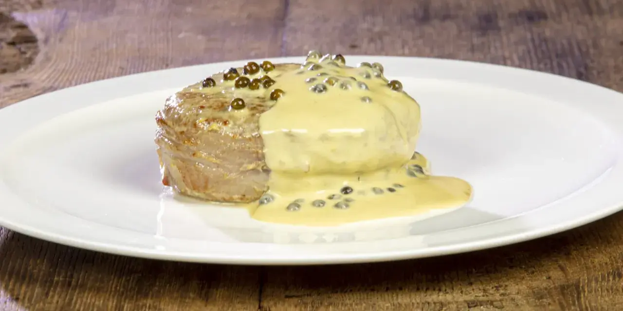 Un succulento filetto al pepe verde, ricoperto da una cremosa salsa, servito su un piatto bianco.