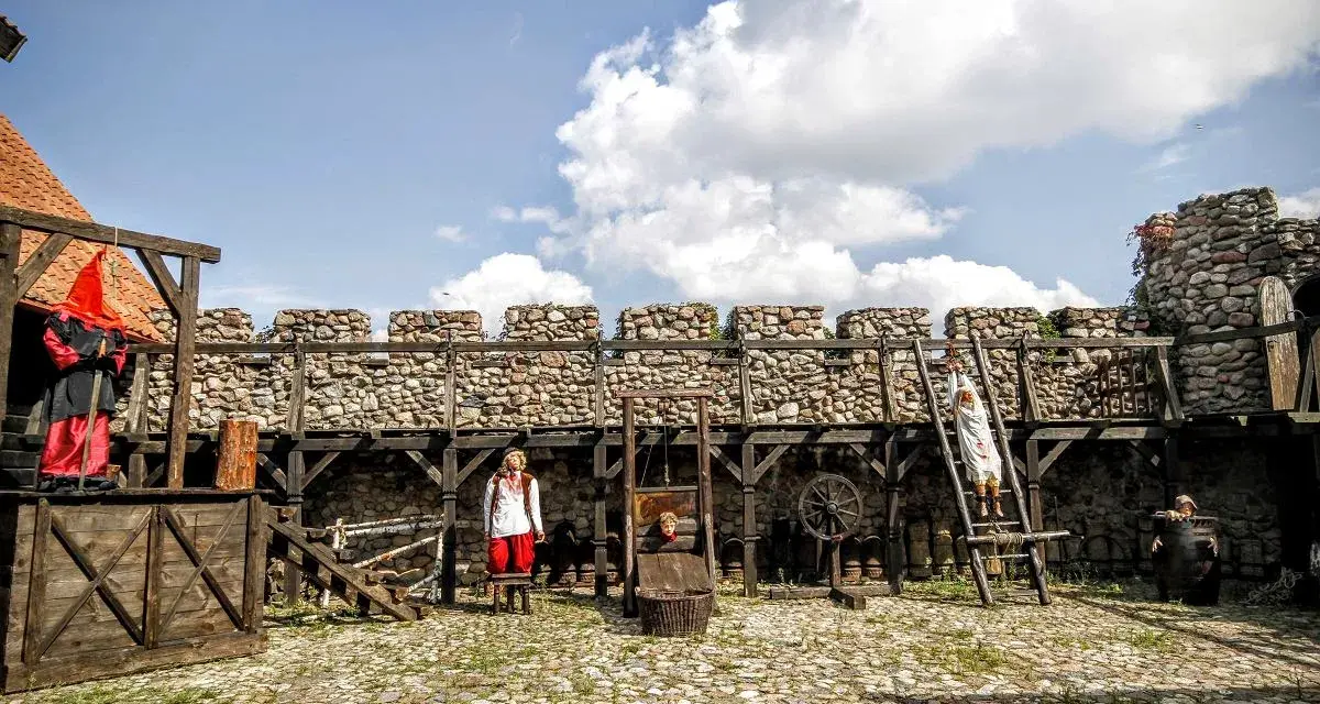Scena z Muzeum Tortur w Krakowie: gilotyna, postacie w strojach historycznych i kamienne mury.