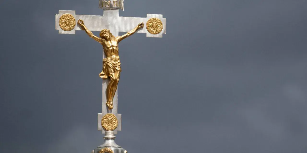 Ein goldenes Kruzifix mit Jesus vor dramatischem Himmel. Die Frage, wie lange dauert die Osterzeit, hallt nach.