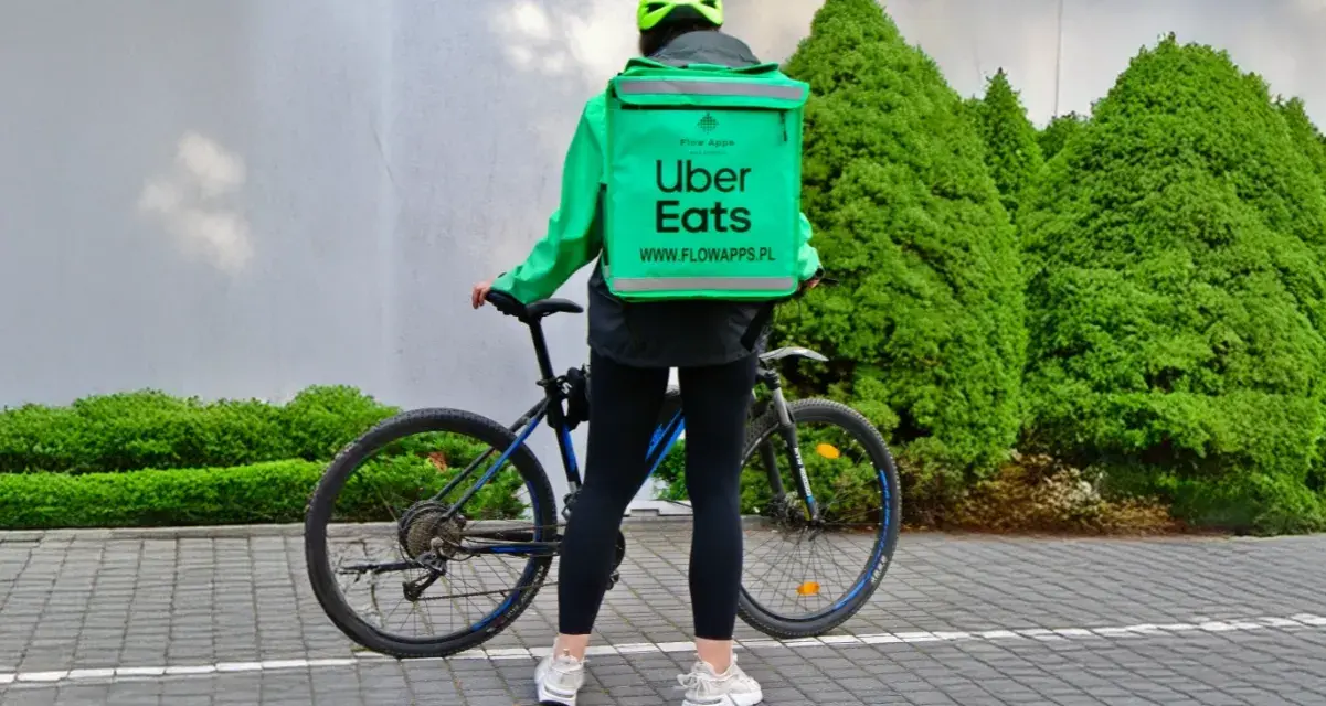 Dostawca Uber Eats w zielonej kurtce i kasku stoi obok roweru.