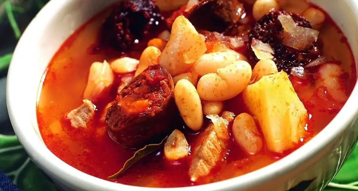 Un reconfortante plato de alubias con chorizo, trozos de morcilla y patatas en un caldo rojizo.